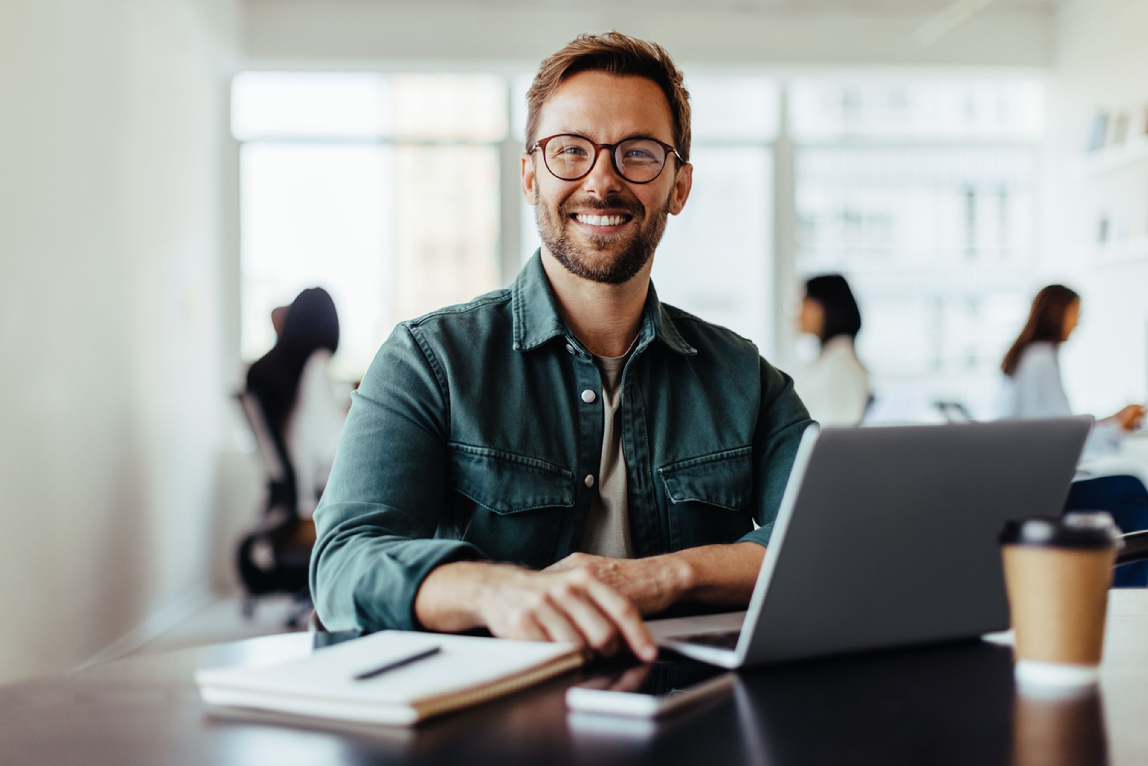 Portrait of a startup employee sitting in an office with his colleagues in the background.
