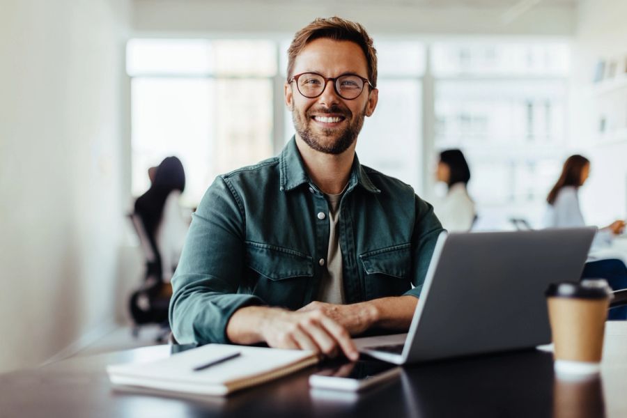 Portrait of a startup employee sitting in an office with his colleagues in the background.