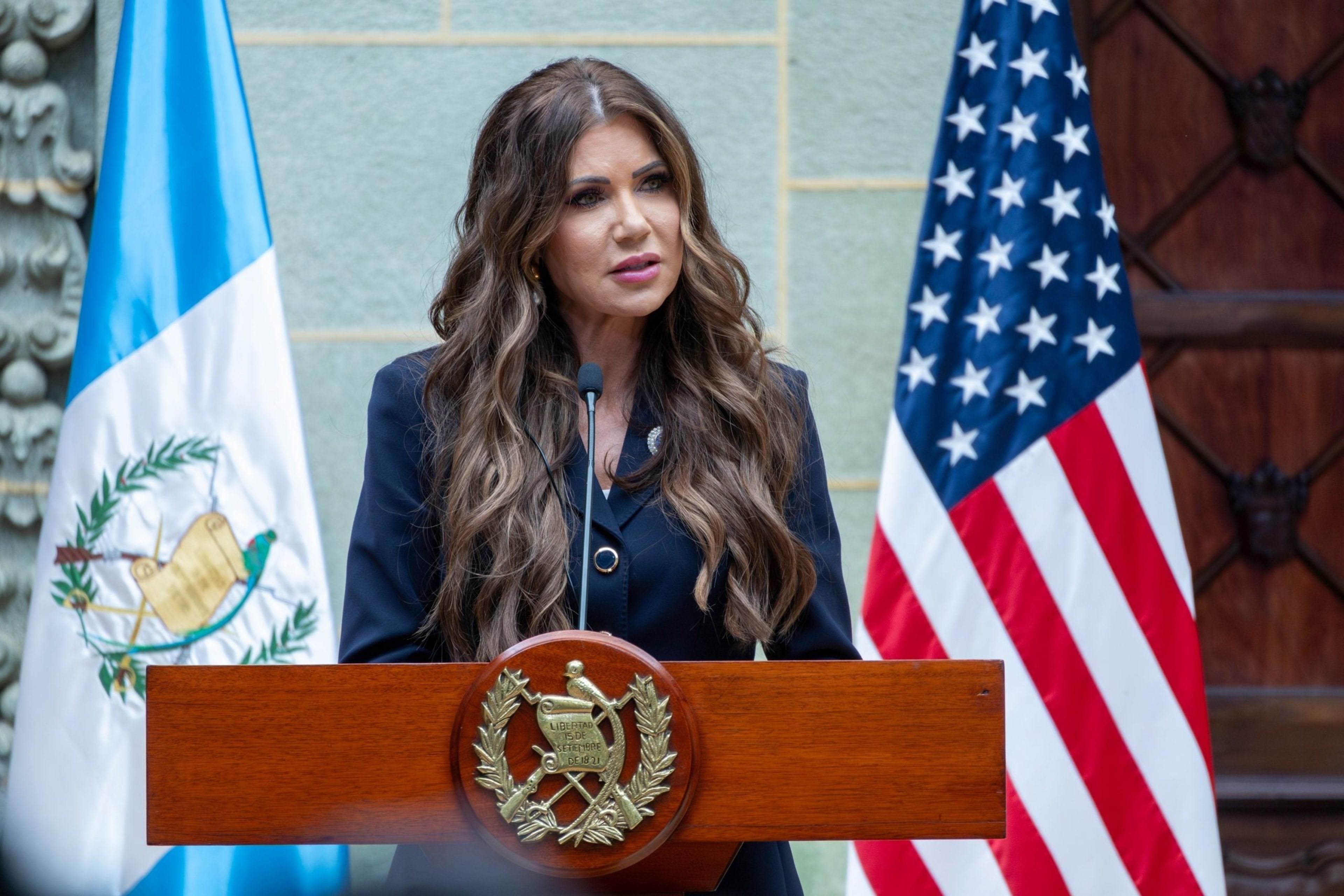 DHS Secretary Kristi Noem standing at a podium flanked by American and Guatemalan flags