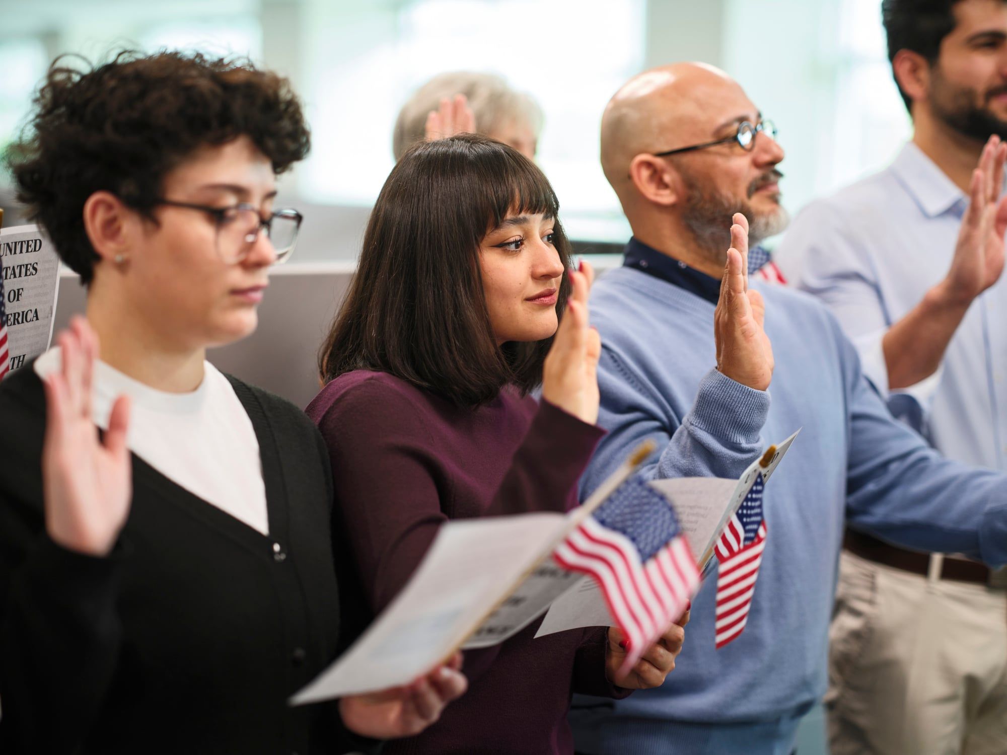 A group of people stands with one hand in the air as they take the Oath of Allegiance to become U.S. citizens.