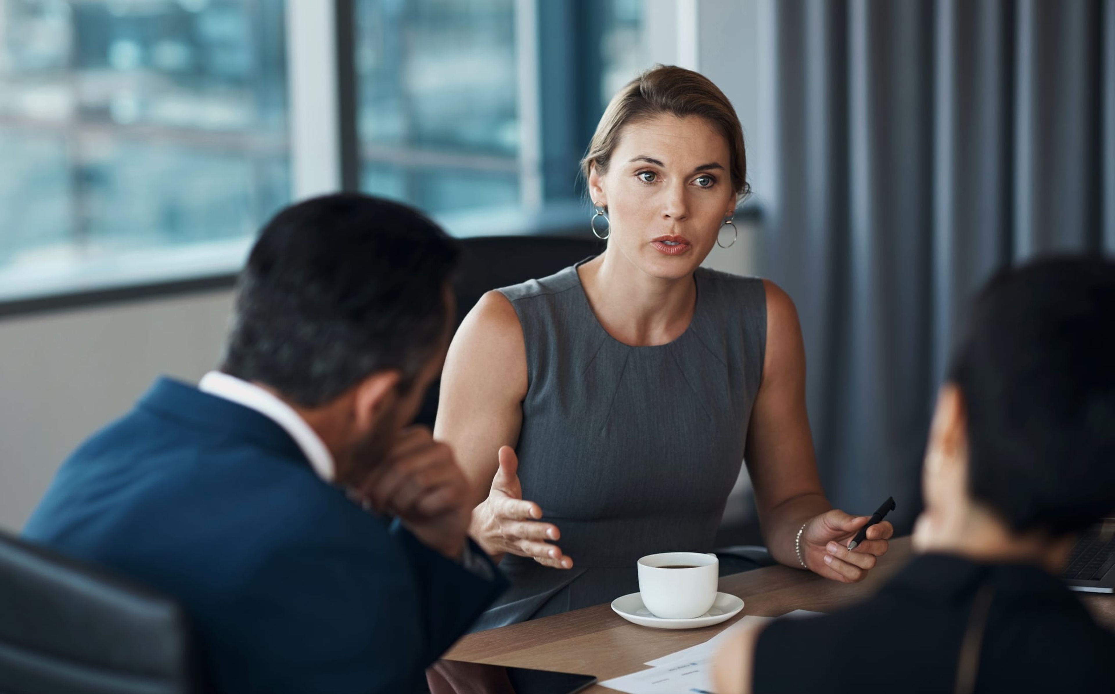 A woman lawyer sits at a desk and talks seriously to multiple clients.