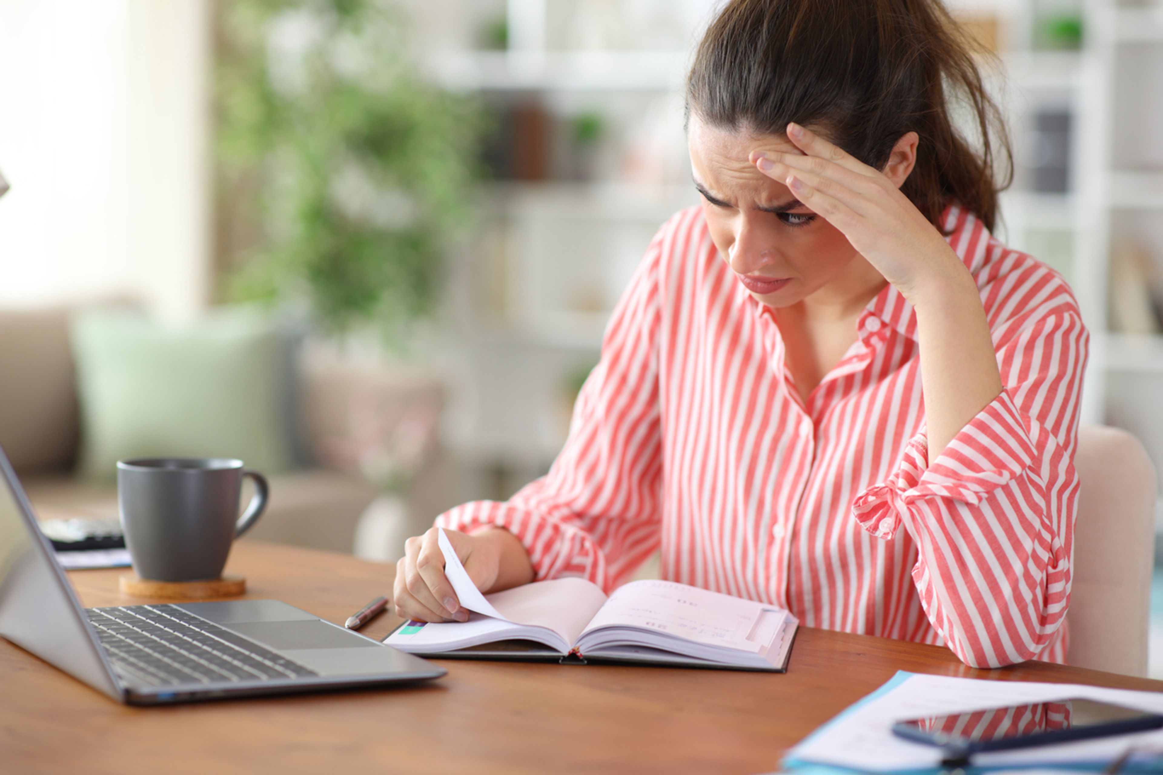 Worried woman consulting laptop and agenda working at home