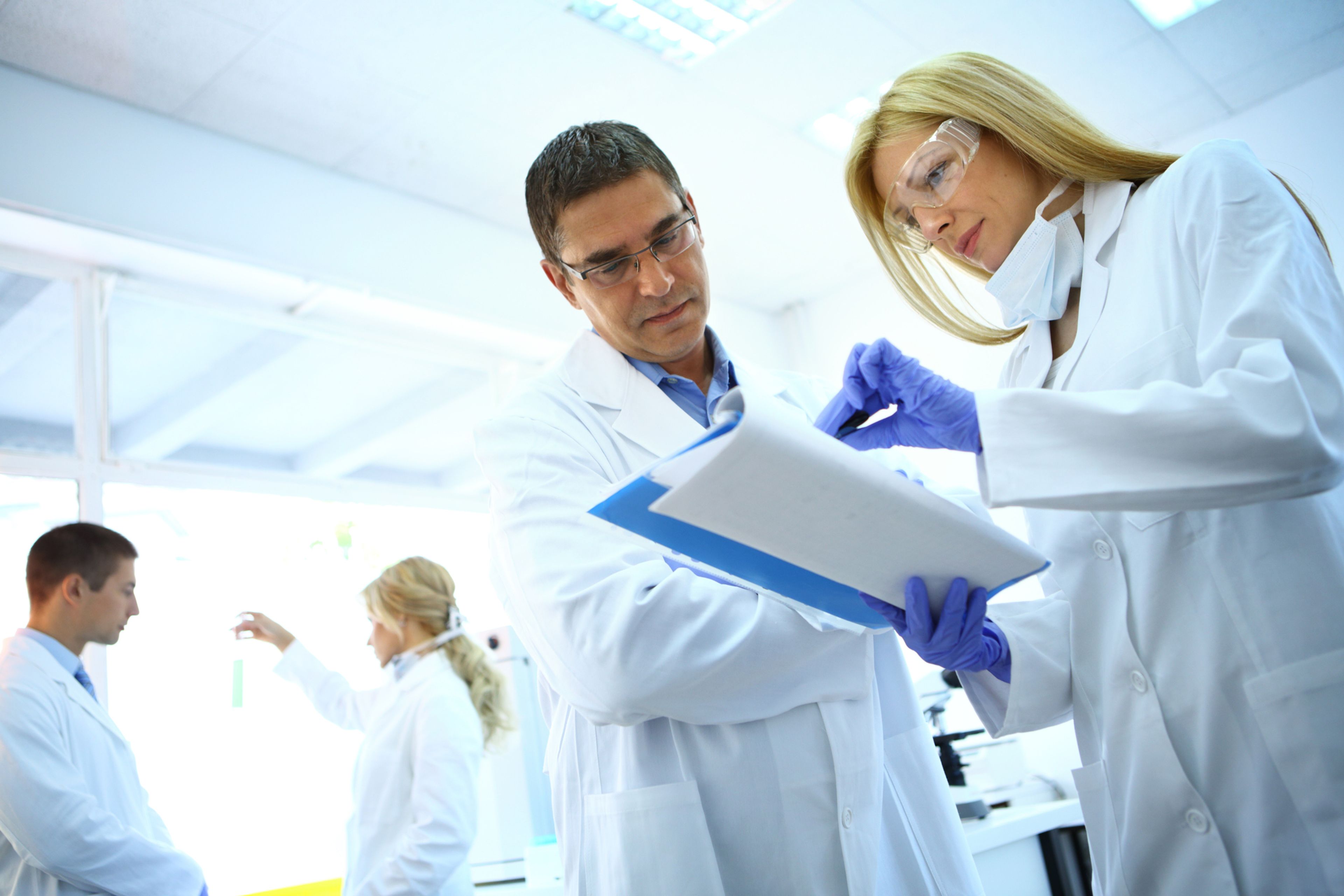 Researchers in white lab coats reviewing notes together in a laboratory.