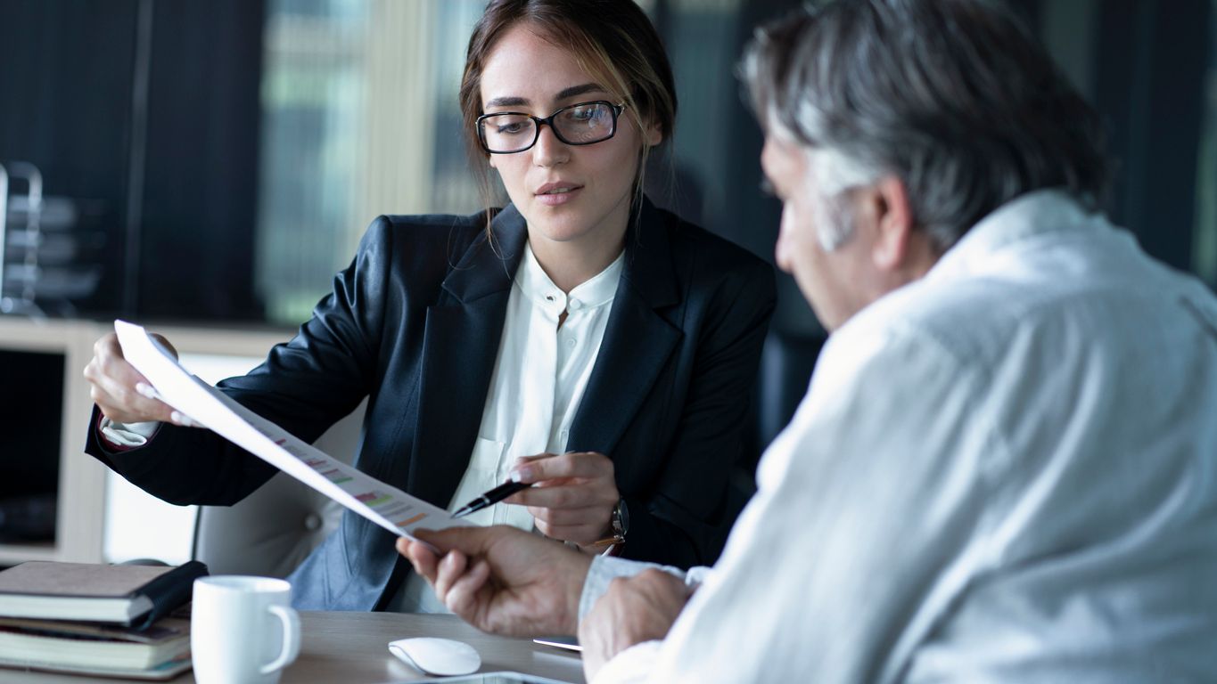 A young business woman shows an older man some financial projections.
