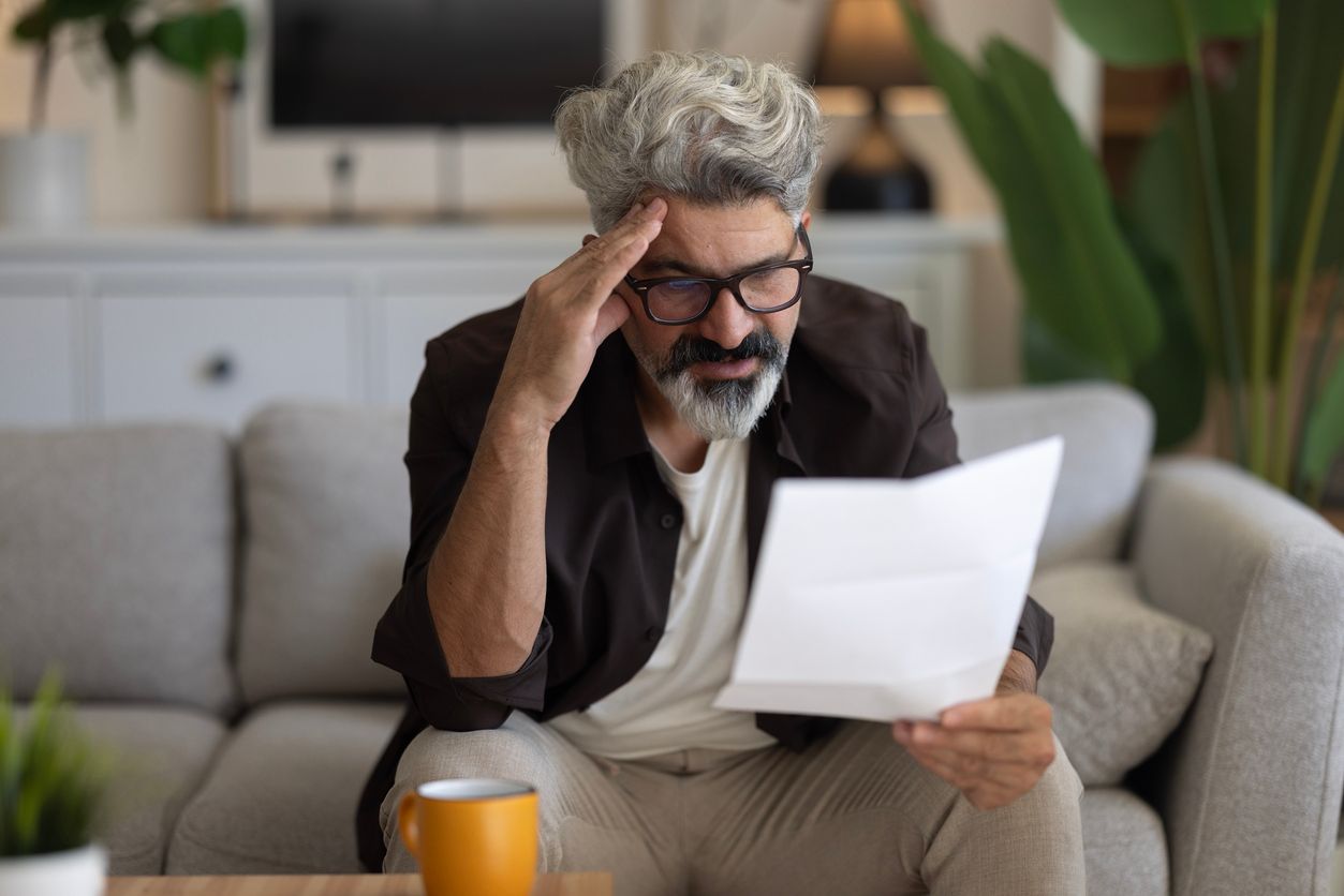 A frustrated man sits on the couch reading a letter.