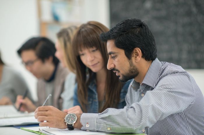 A man and woman sit at a table looking at paperwork, with other consultants in the background.