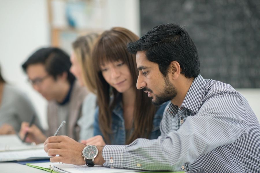 A man and woman sit at a table looking at paperwork, with other consultants in the background.