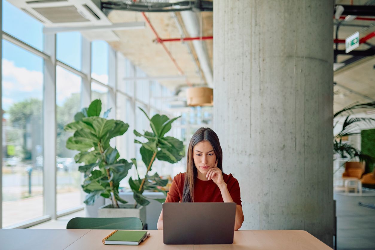 Young businesswoman concentrating while using laptop at desk in bright, modern office space.