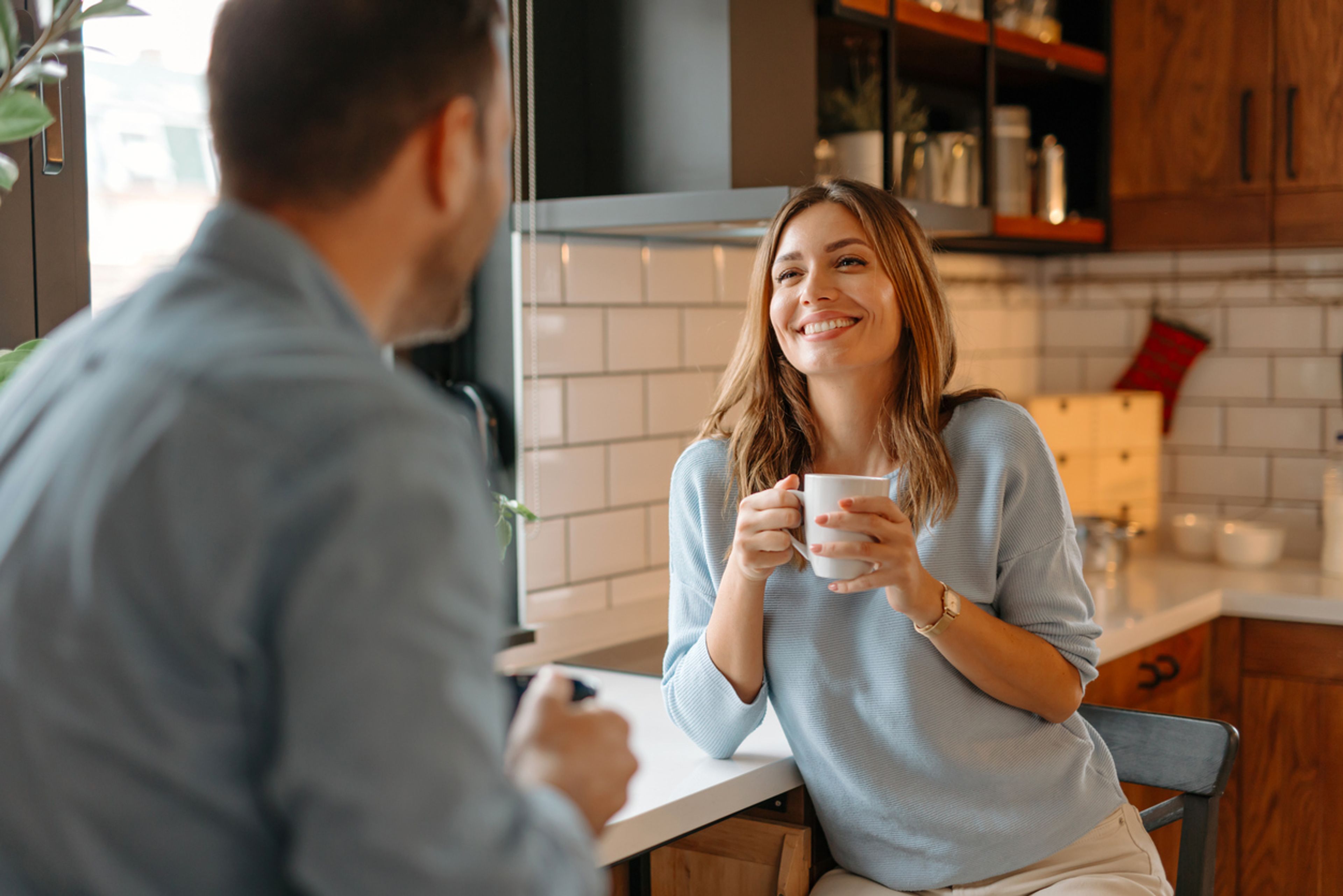 Young married couple smiling at each other in their kitchen.