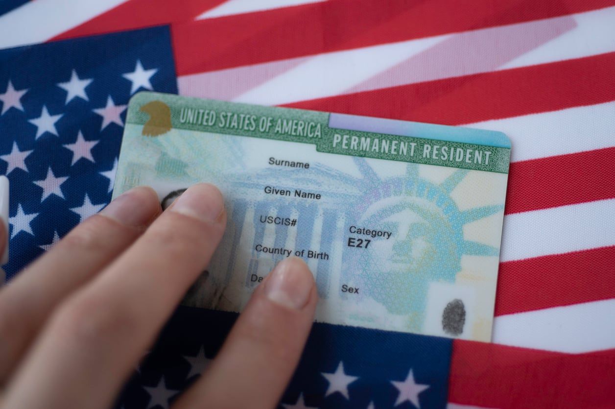 Closeup of Green Card against American flag backdrop.