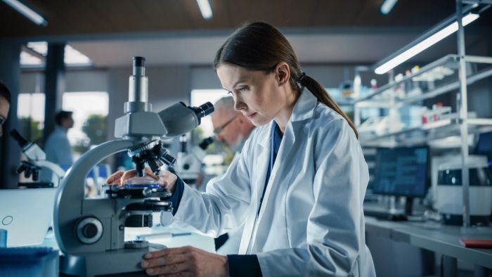 Bioengineer looking at DNA samples under a microscope in her lab.