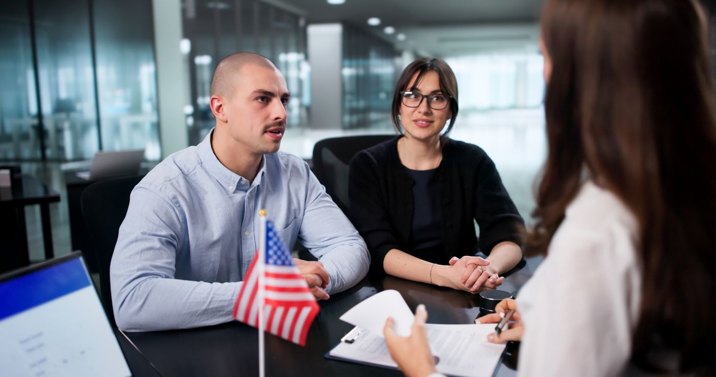 A man and woman sit in front of a desk during an interview with a consular officer.