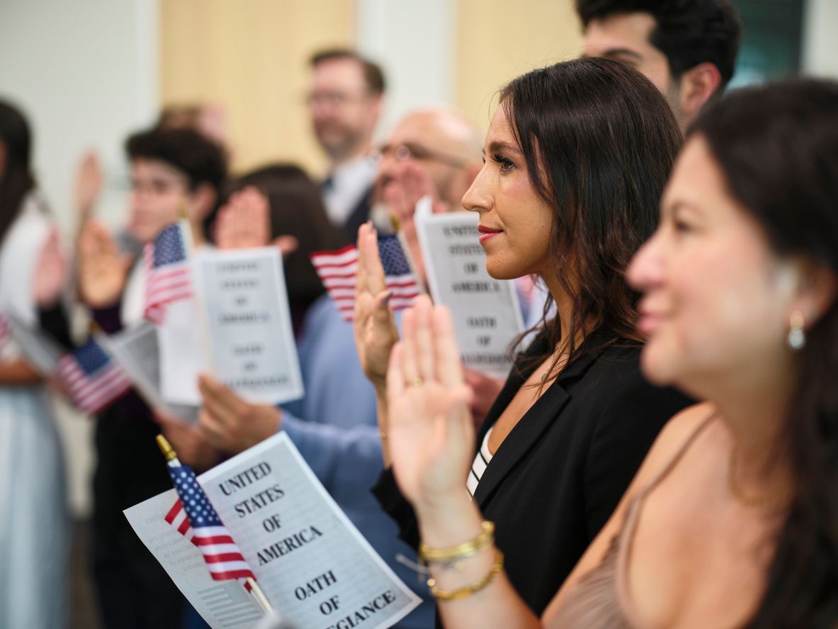A diverse group of people in a ceremony taking the United States Naturalization Oath of Allegiance to become citizens.