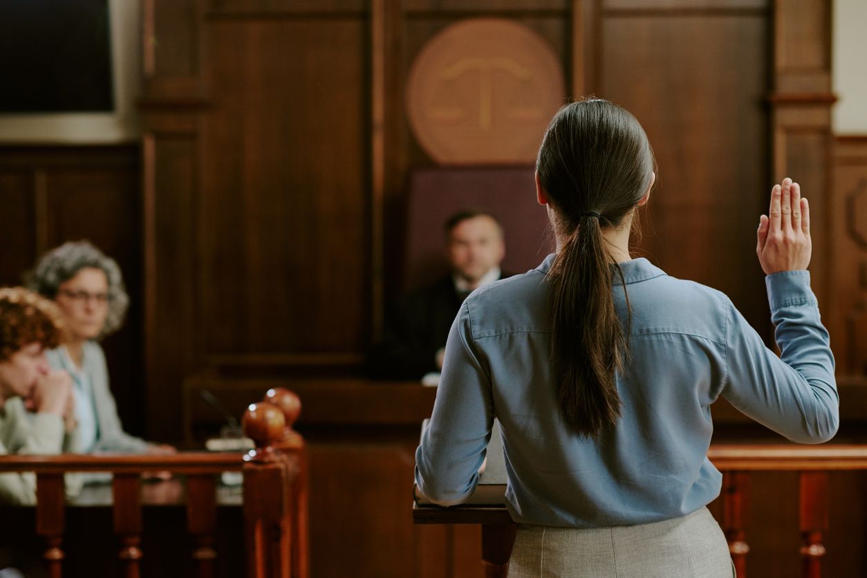 Person standing in courtroom raising right hand while swearing oath.
