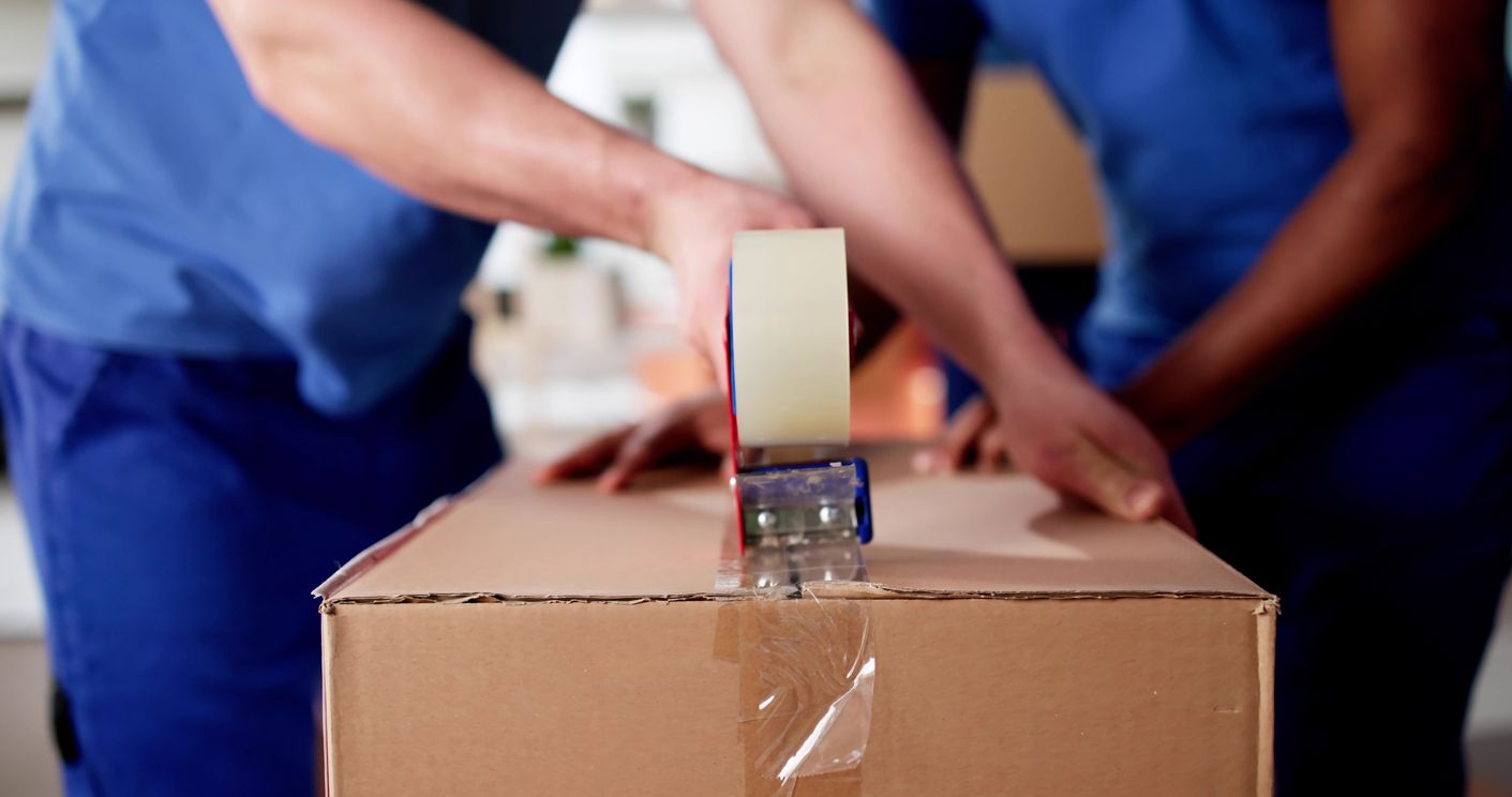 Professional movers pack cardboard boxes with tape.