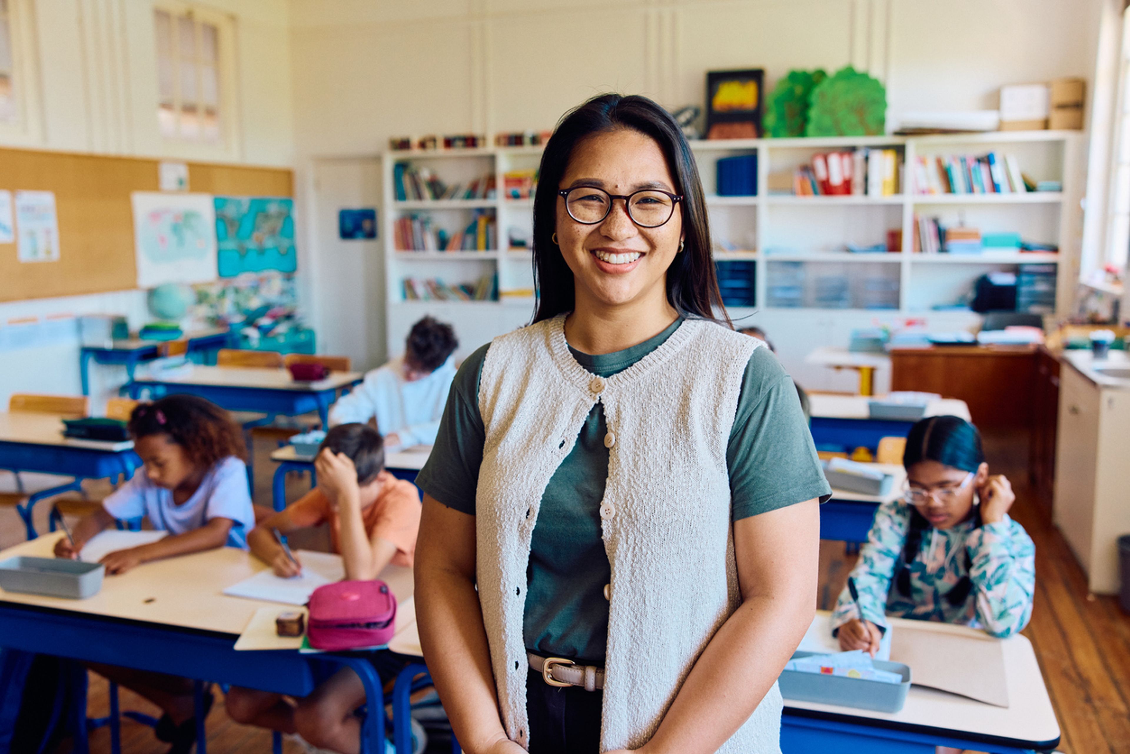A woman teacher stands smiling in front of a classroom full of young children.