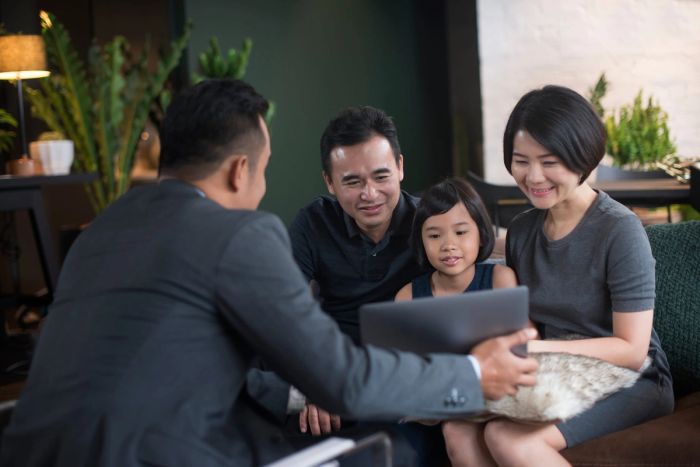 An attorney shows a man, woman, and child a laptop screen while explaining their immigration options on an L-2 visa.