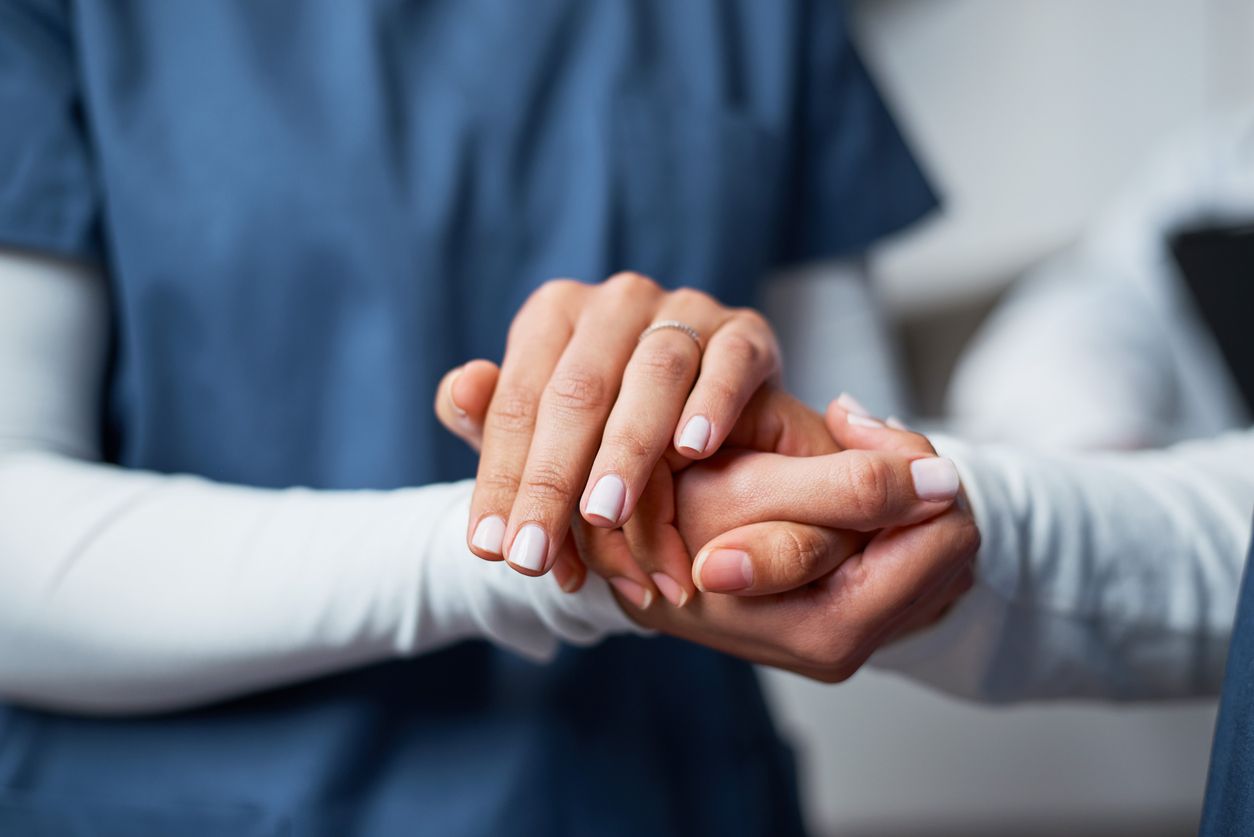 A nurse provides emotional support by gently holding a patient's hand.