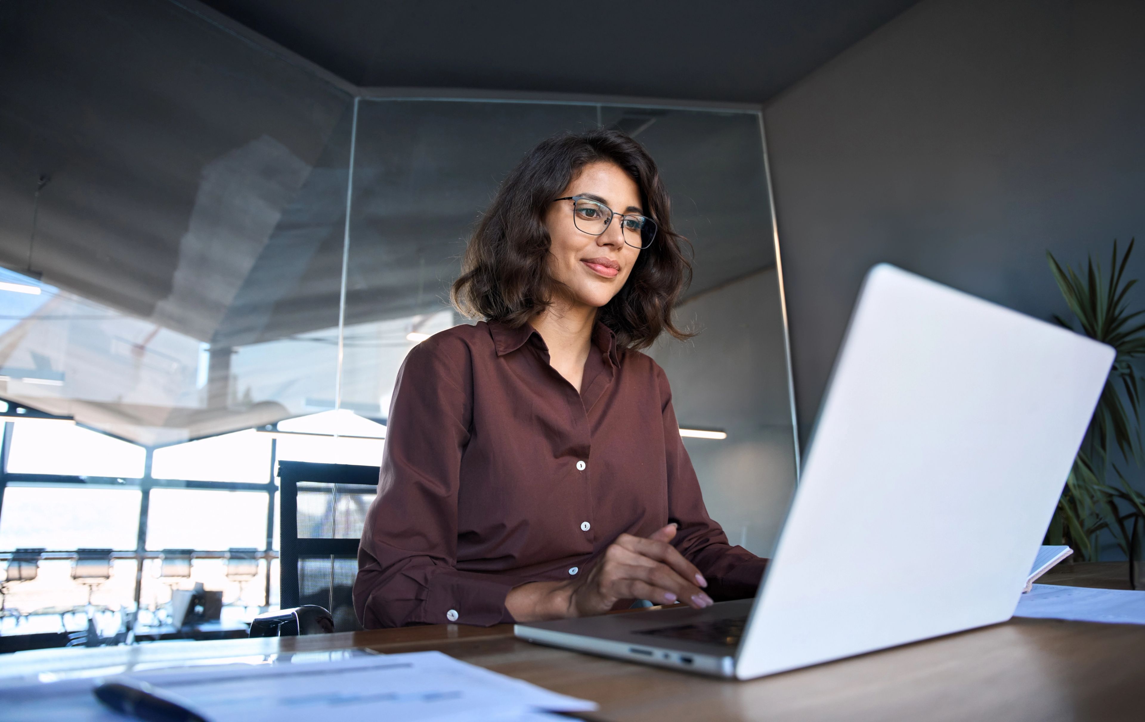 a person with long brown hair and glasses types on a laptop