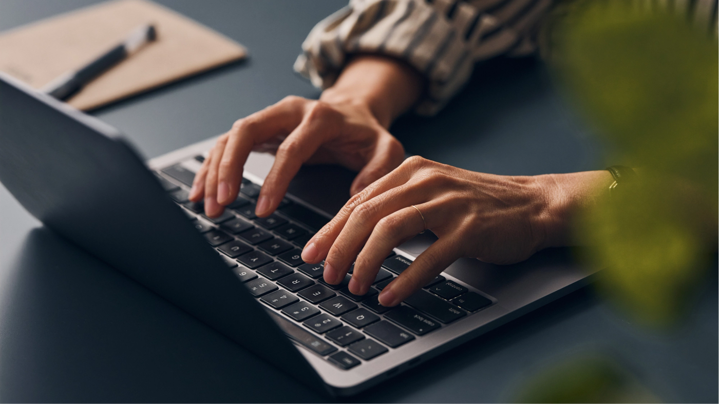 Close-up of hands typing on a laptop at a desk