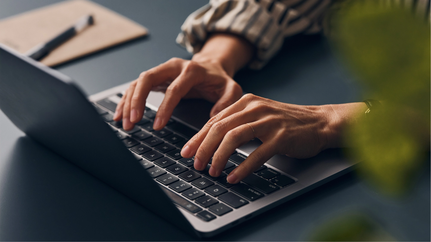 Close-up of hands typing on a laptop at a desk