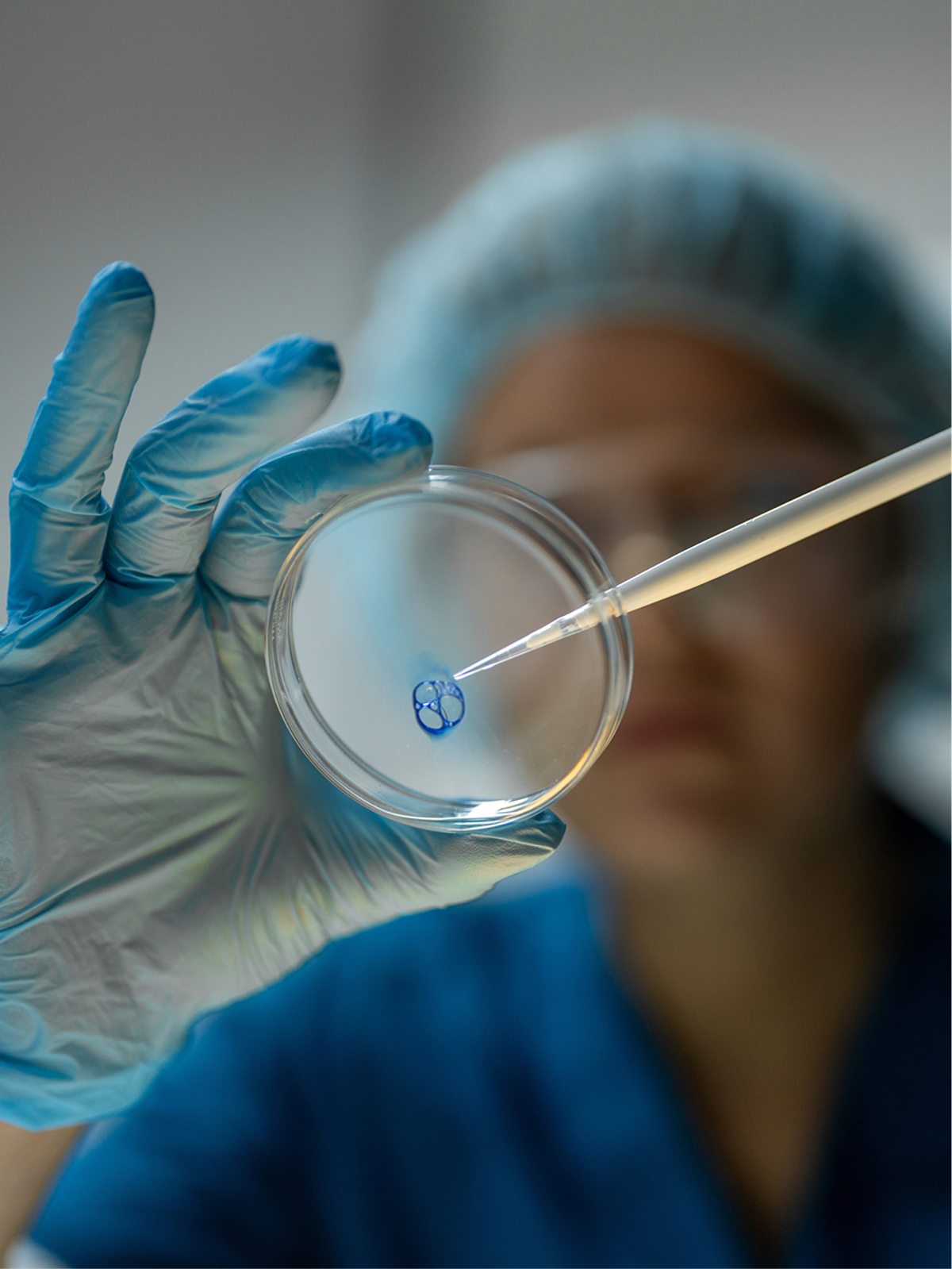 A researcher pipetting blue liquid into a petri dish in a lab