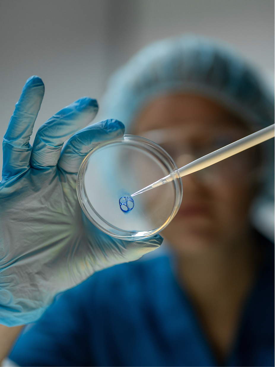 A researcher pipetting blue liquid into a petri dish in a lab