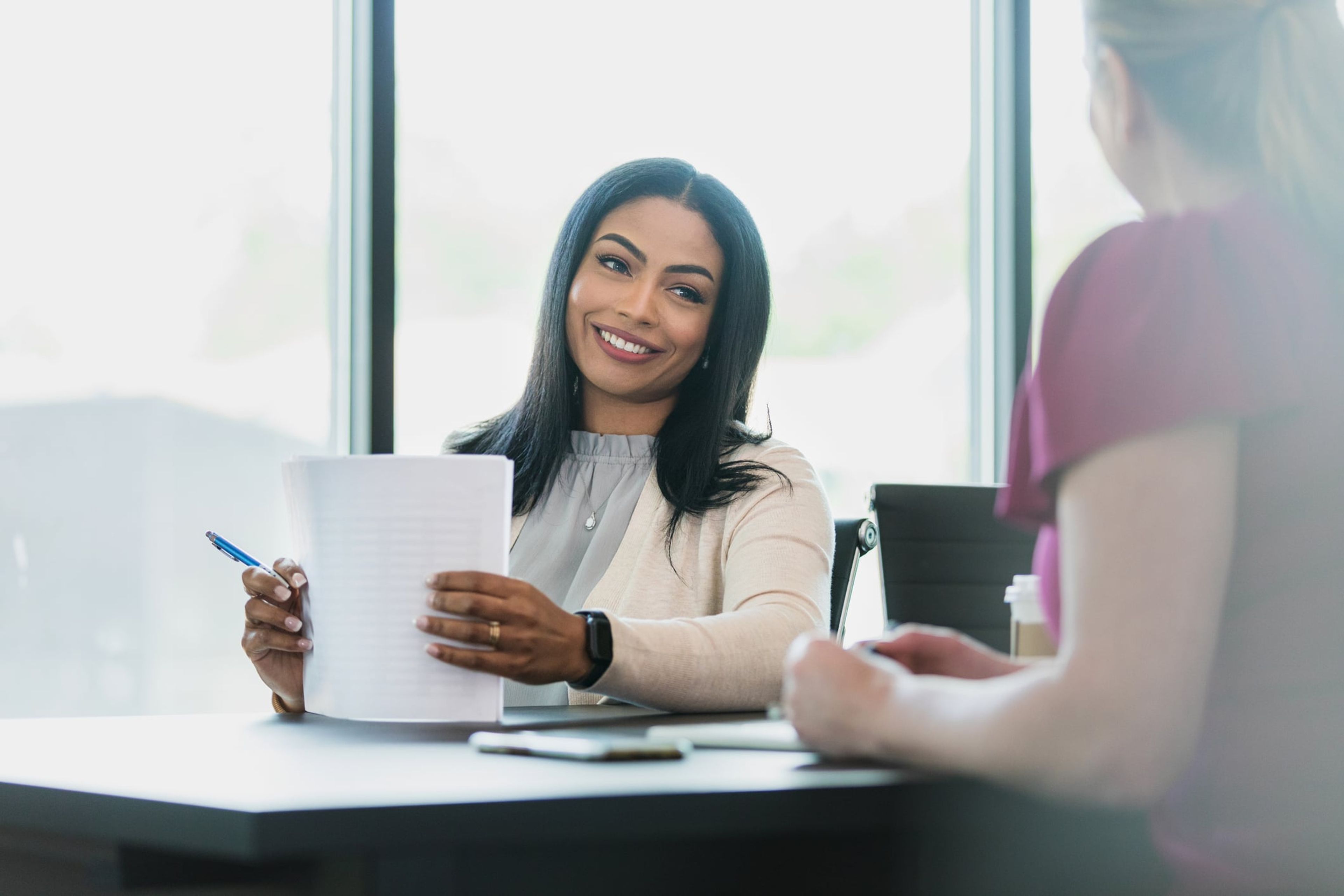 A female boss smiles at her employee while holding an employment verification letter.