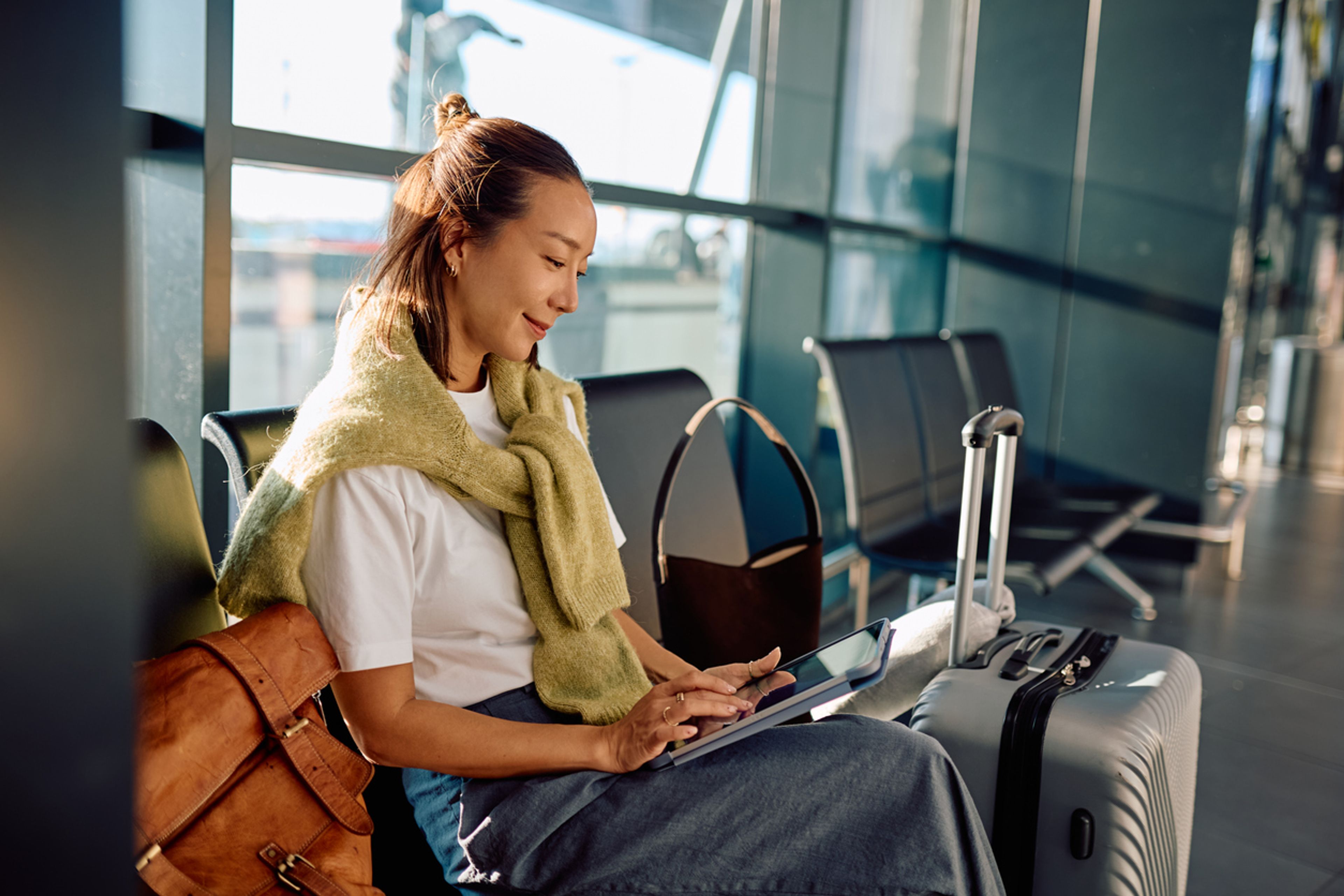 woman traveling, sitting in the airport waiting area, using tablet computer and waiting for her flight