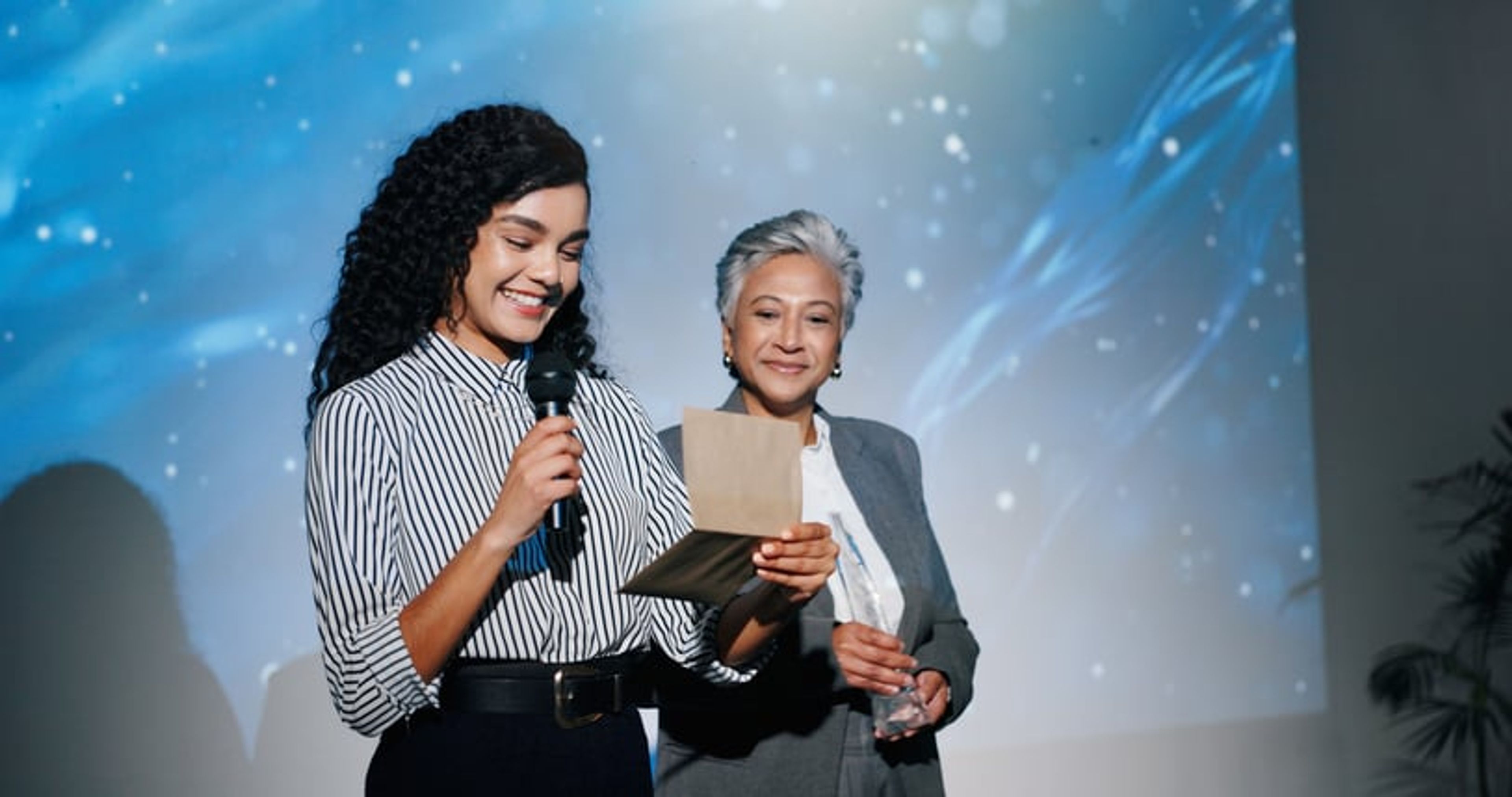 A woman stands with a microphone and a card after accepting an award in the sciences.
