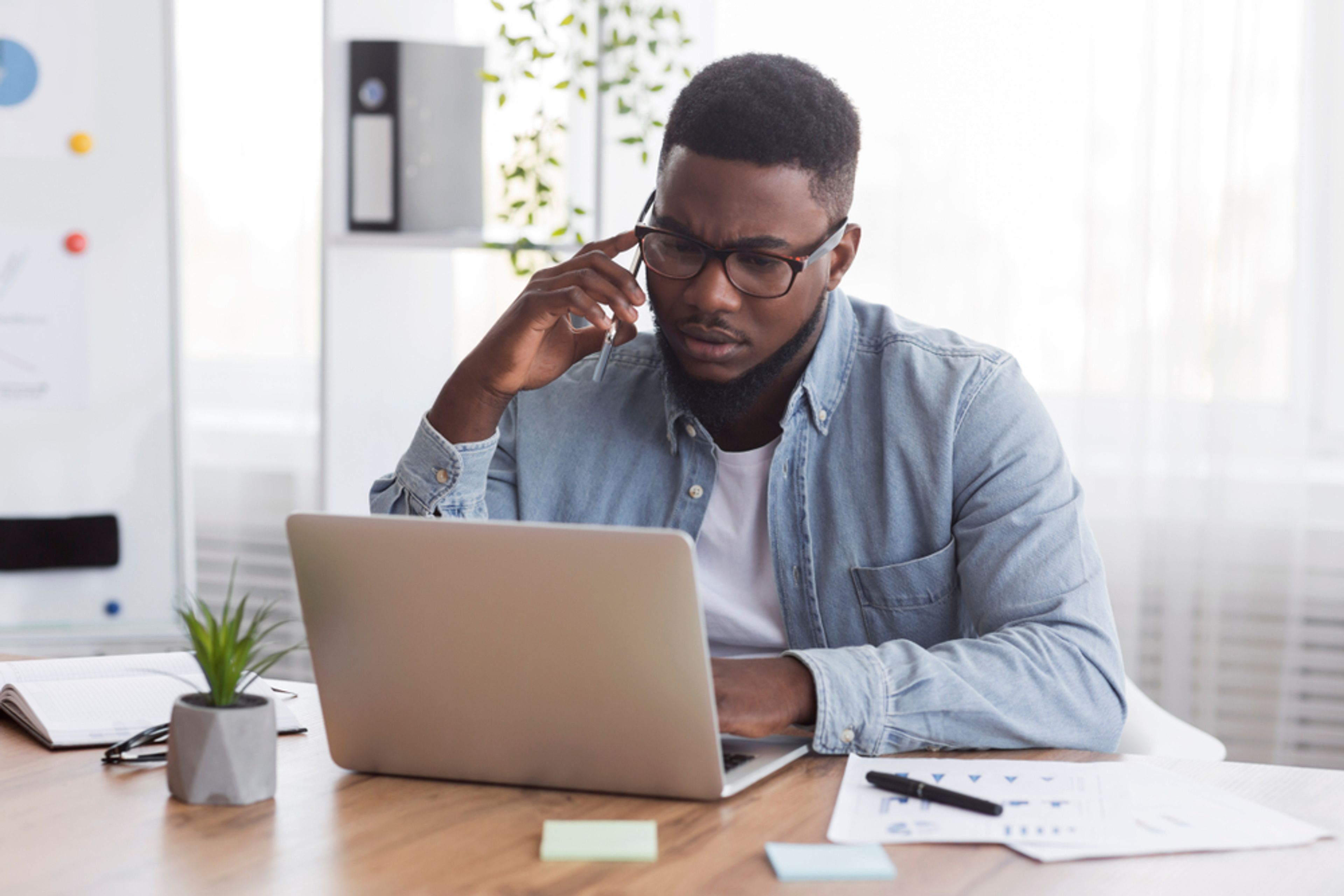 Concerned worker talking on cell phone while looking at laptop screen