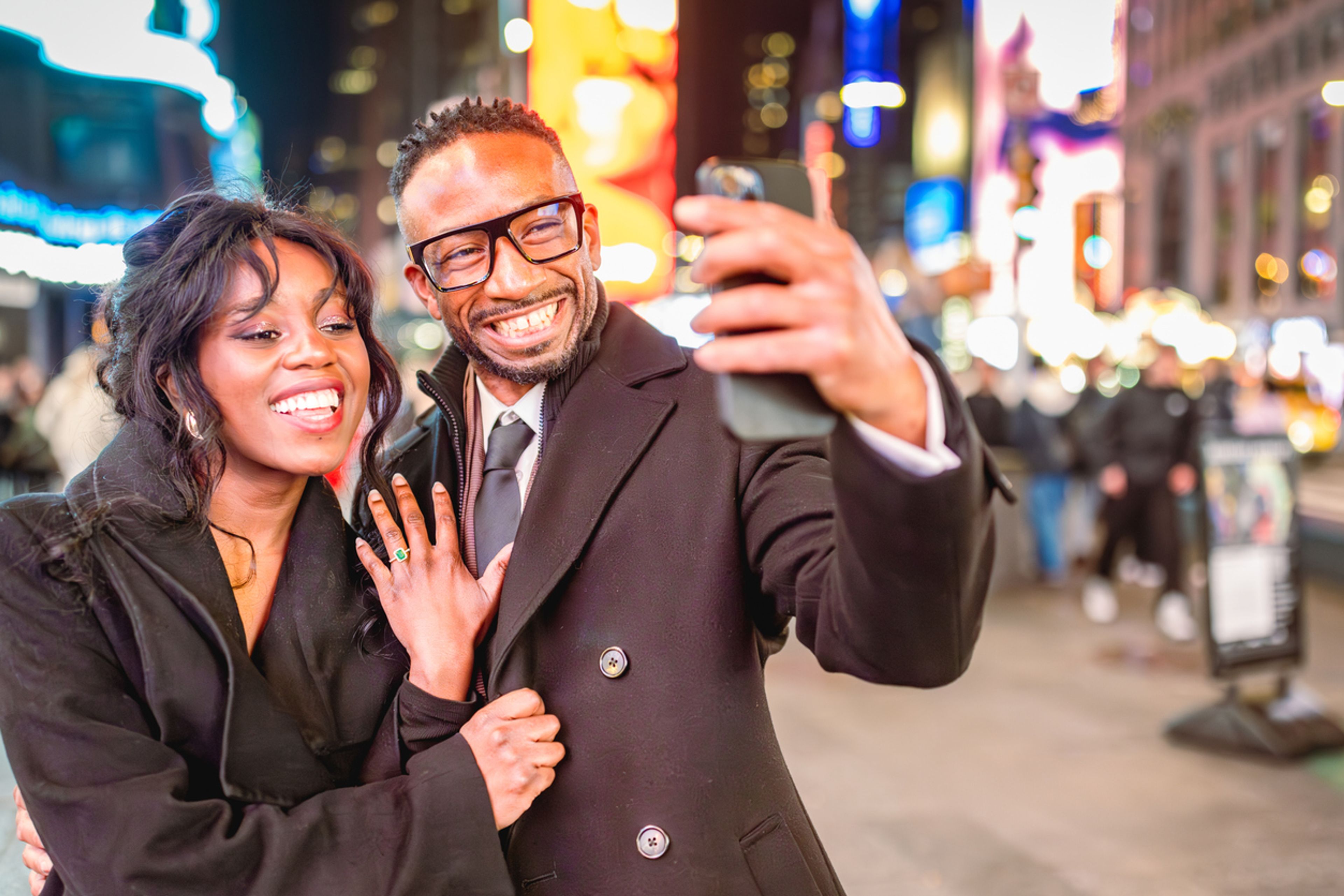 Couple posing in Times Square, New York, showing off a new engagement ring.