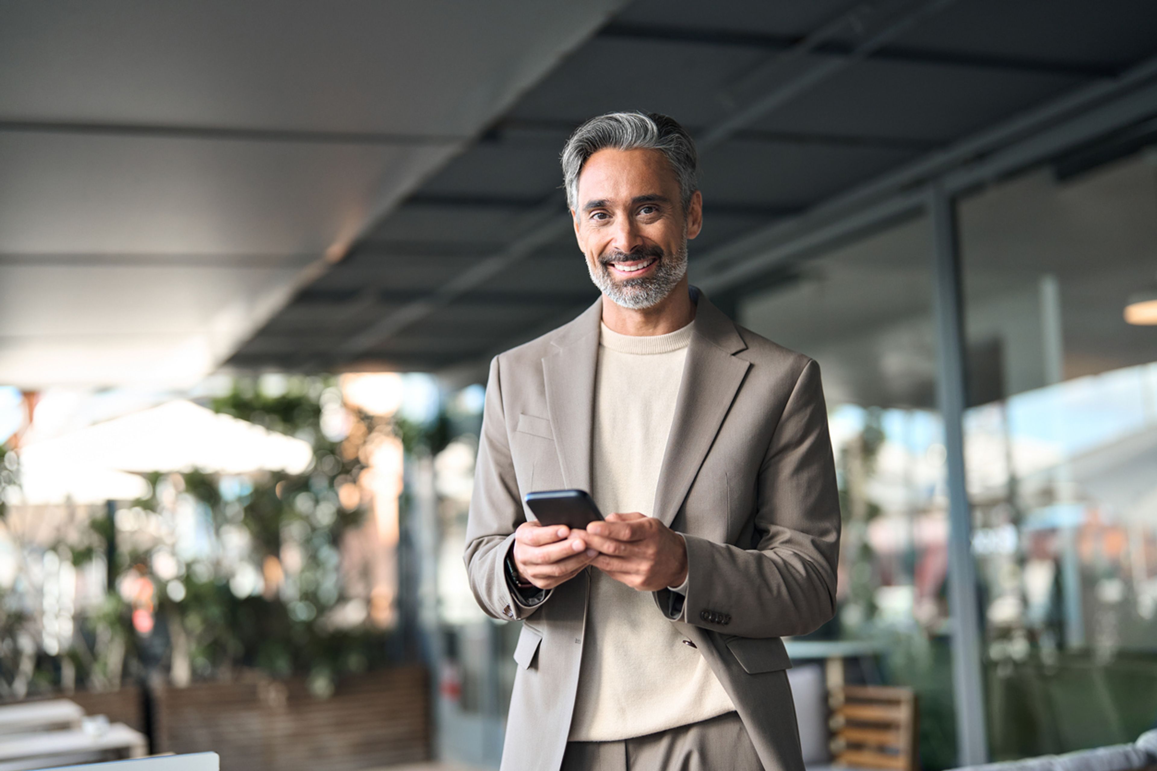 Entrepreneur holding his phone while standing outside and smiling.