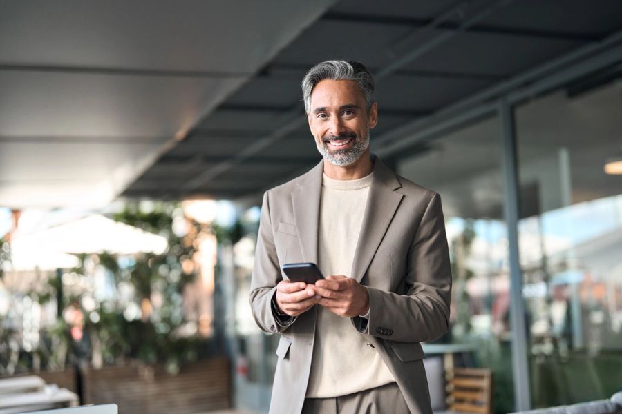 Entrepreneur holding his phone while standing outside and smiling.