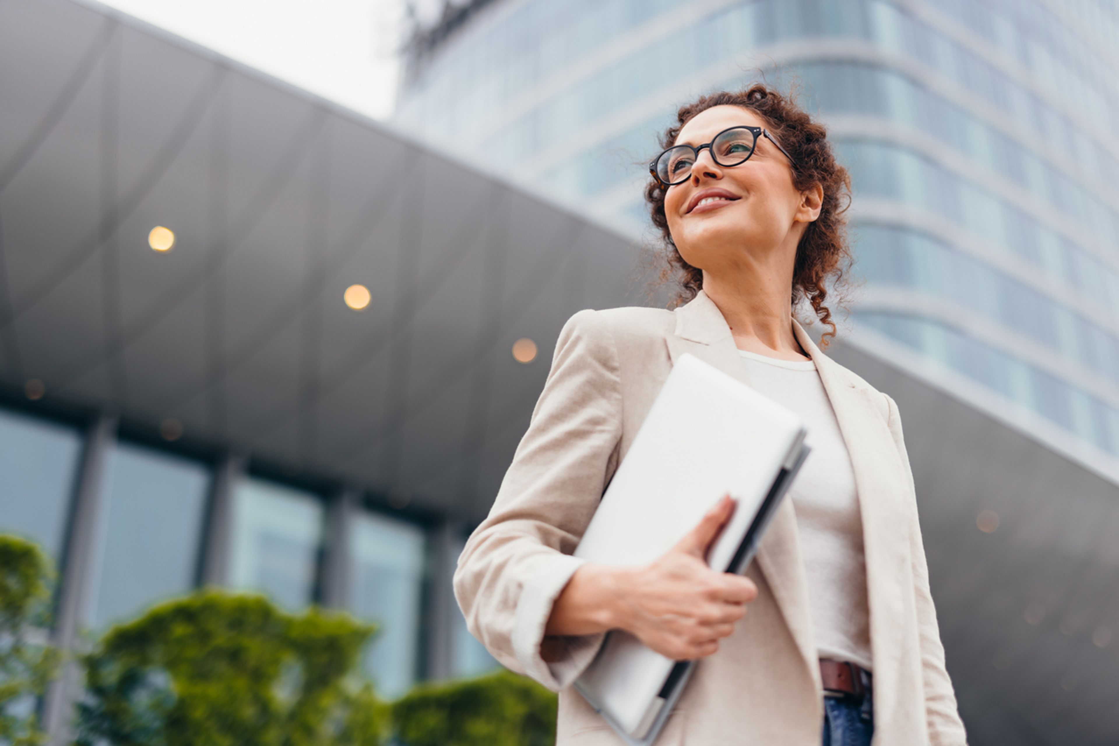 Happy businesswoman in eyeglasses holding a laptop, smiling confidently.
