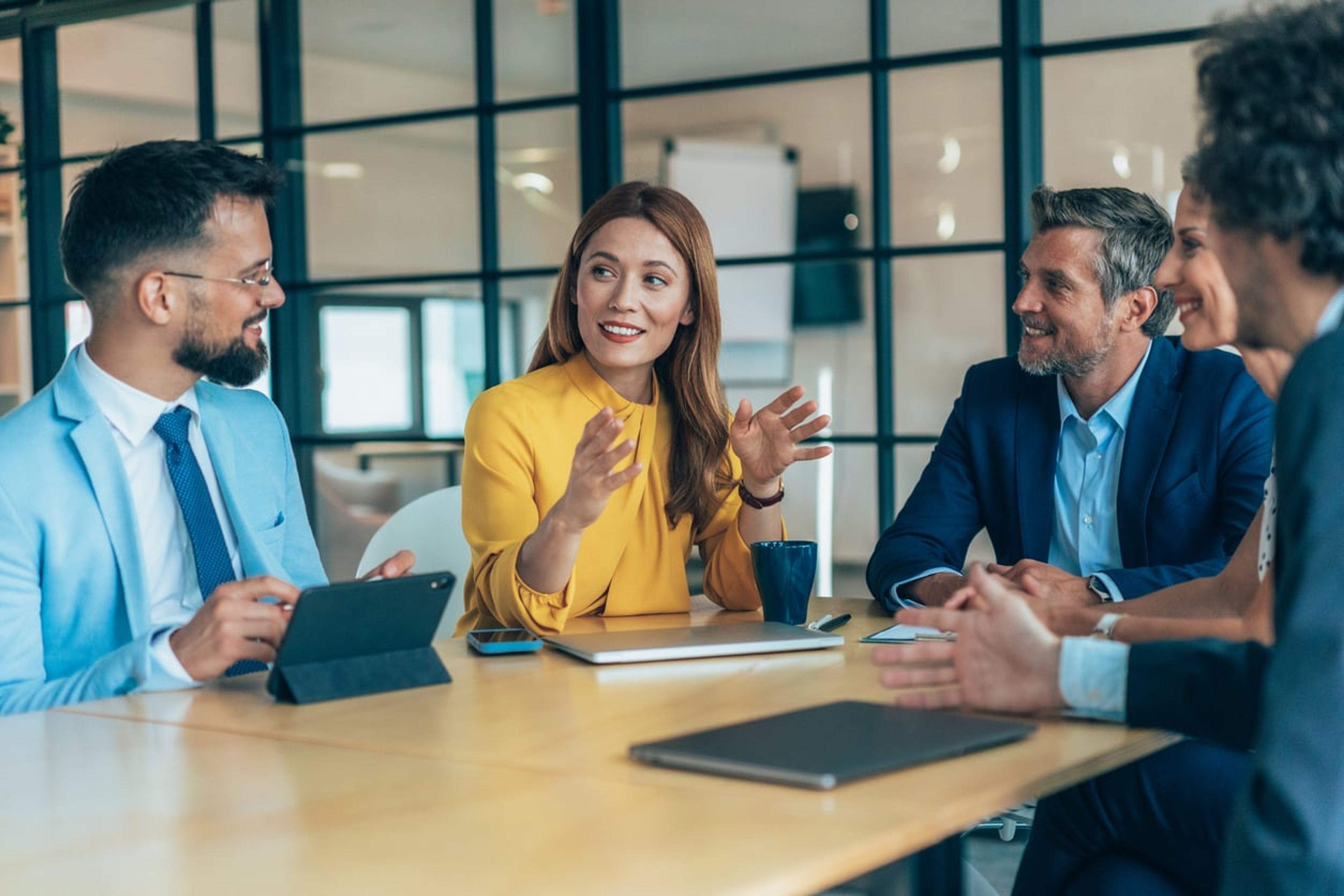 A female company founder sits at a table explaining something to a group of board members.