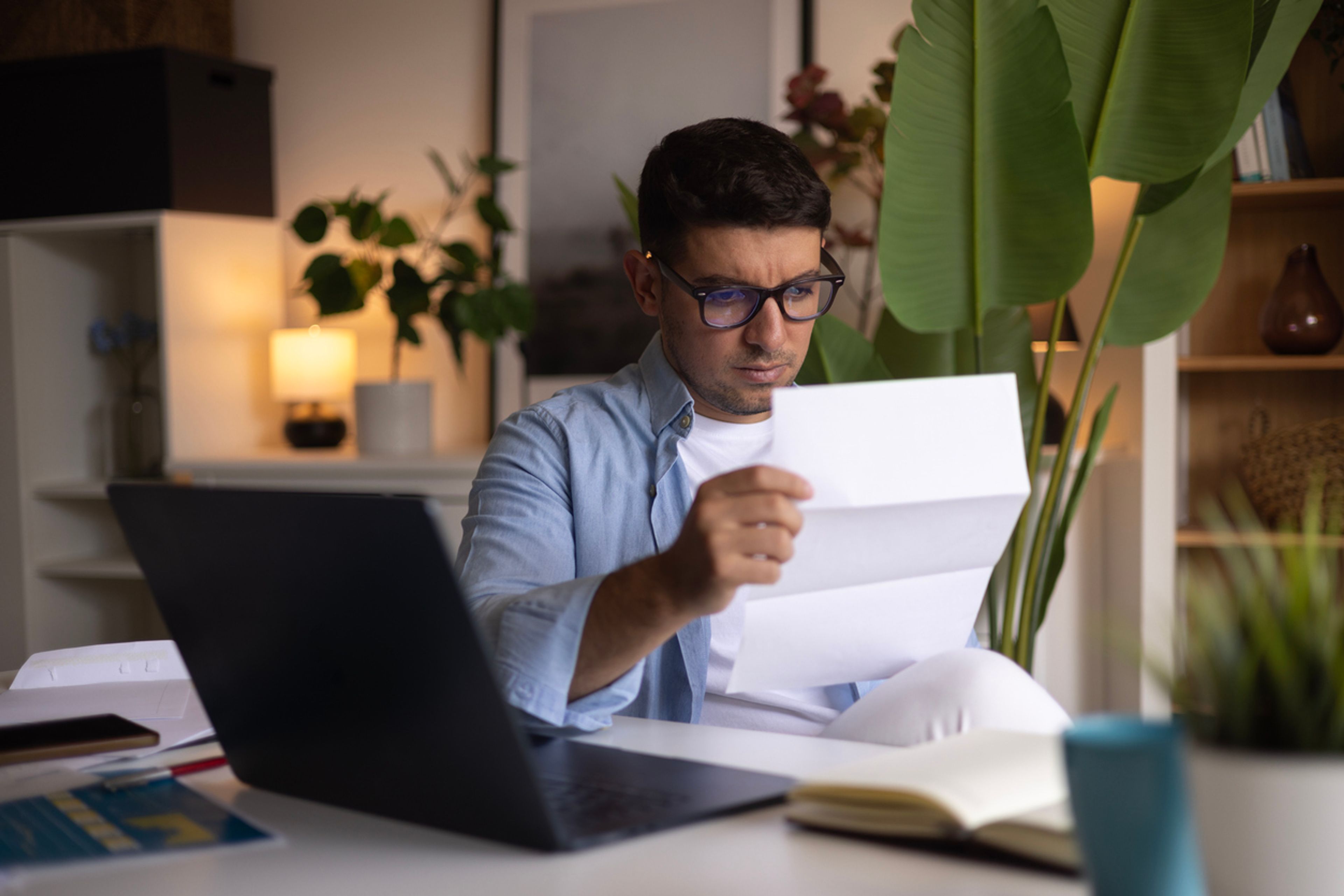 A man sits at a desk and reads a letter with a confused look on his face.