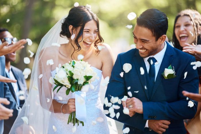 A bride and groom smile at a marriage ceremony while confetti falls on them.