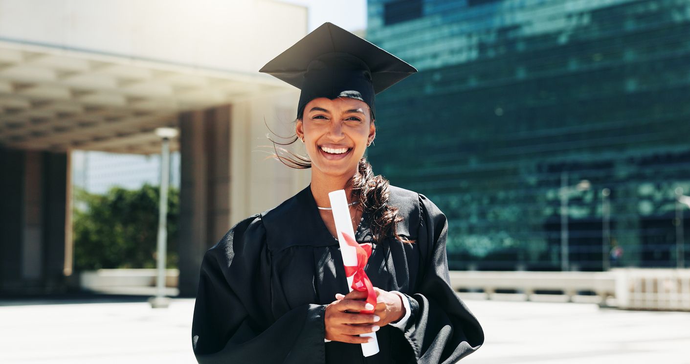 Portrait of a woman wearing graduation cap and gown and holding a diploma.