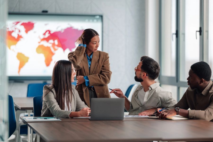 A business team discussing global strategy in a meeting room with a world map on screen.