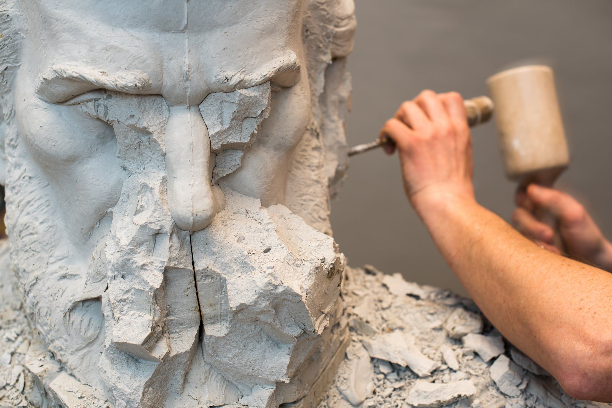 The hands of a sculptor are carving a stone scultpure with a hammer.