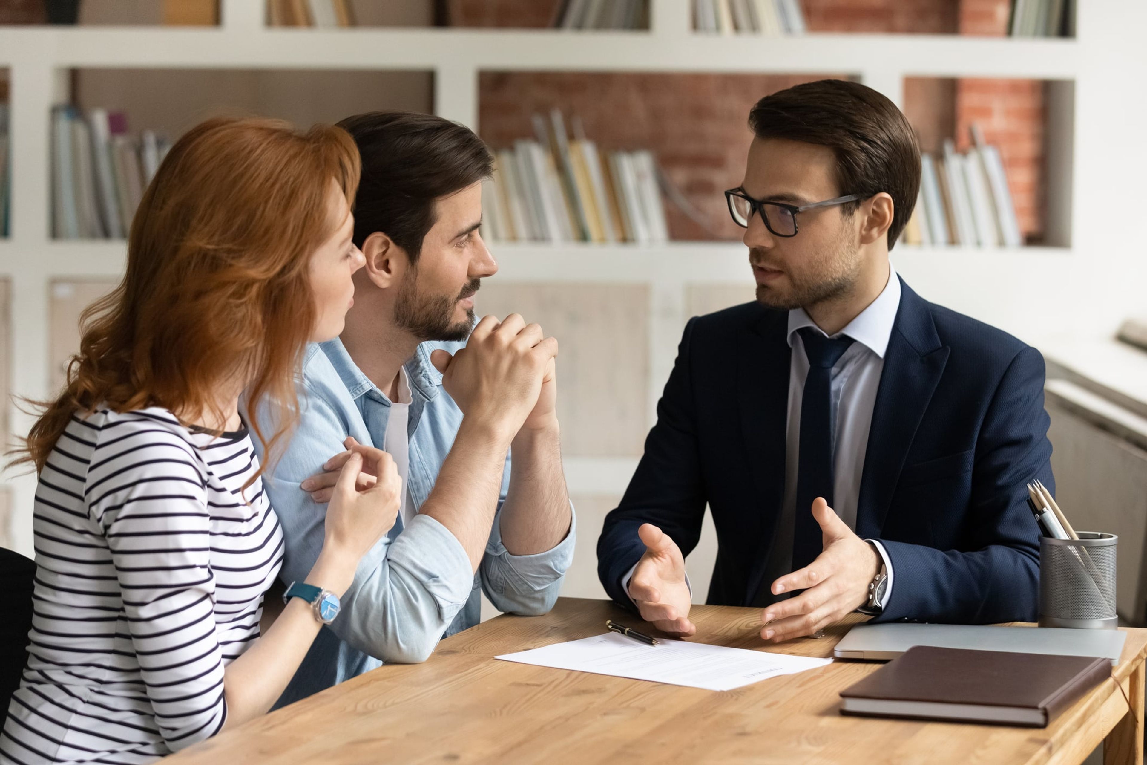 A young couple sits at a desk and listens intently to an immigration attorney who is explaining their visa options during a consulattaion.
