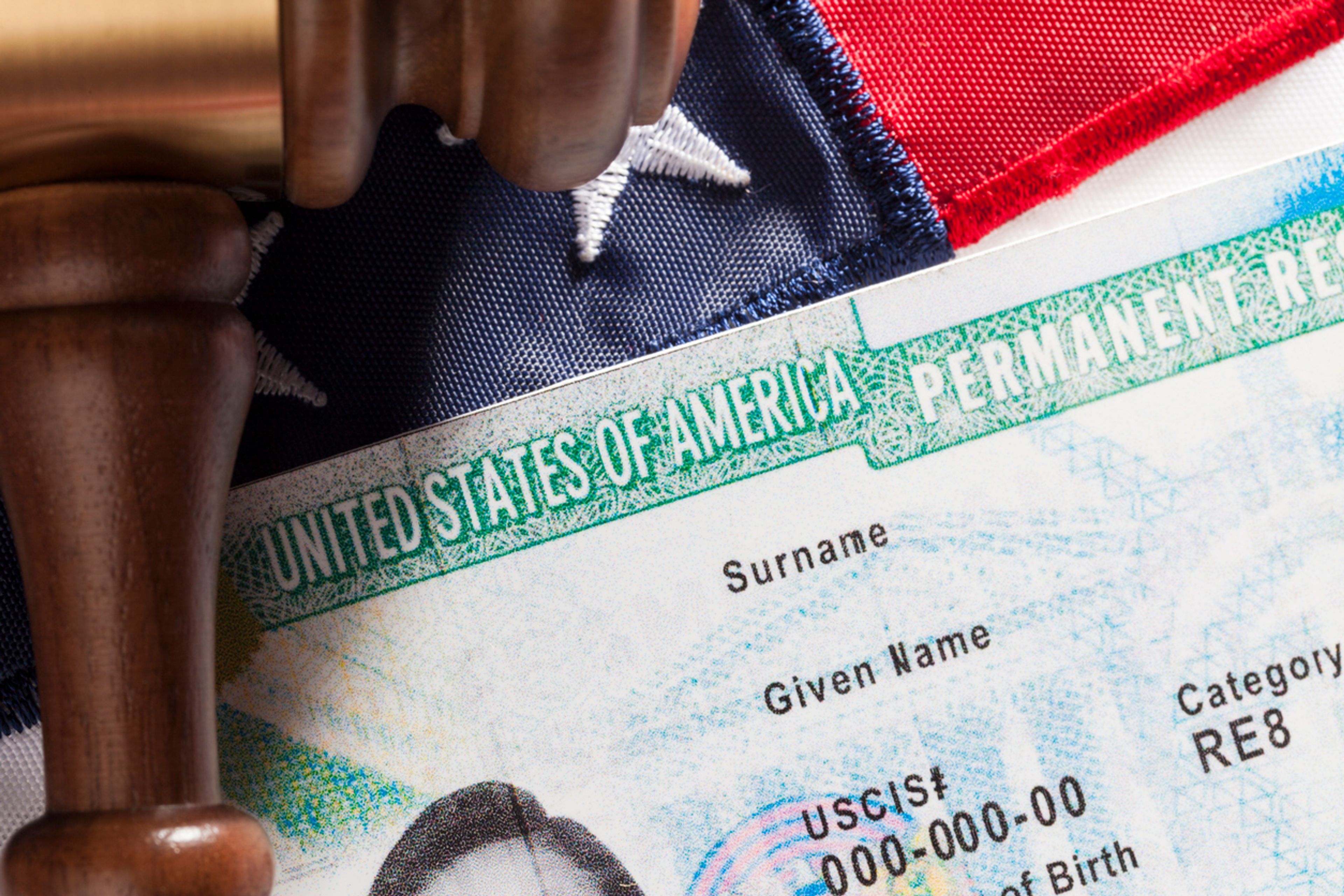 Closeup of a Green Card against an American flag backdrop.