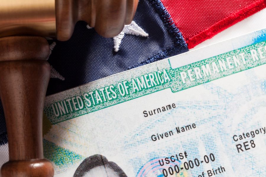 Closeup of a Green Card against an American flag backdrop.