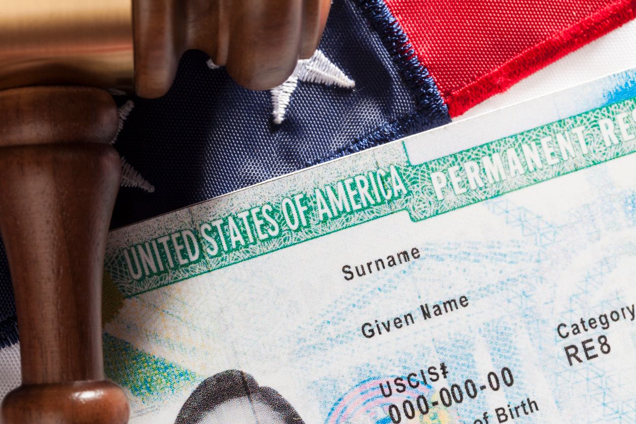Closeup of a Green Card against an American flag backdrop.