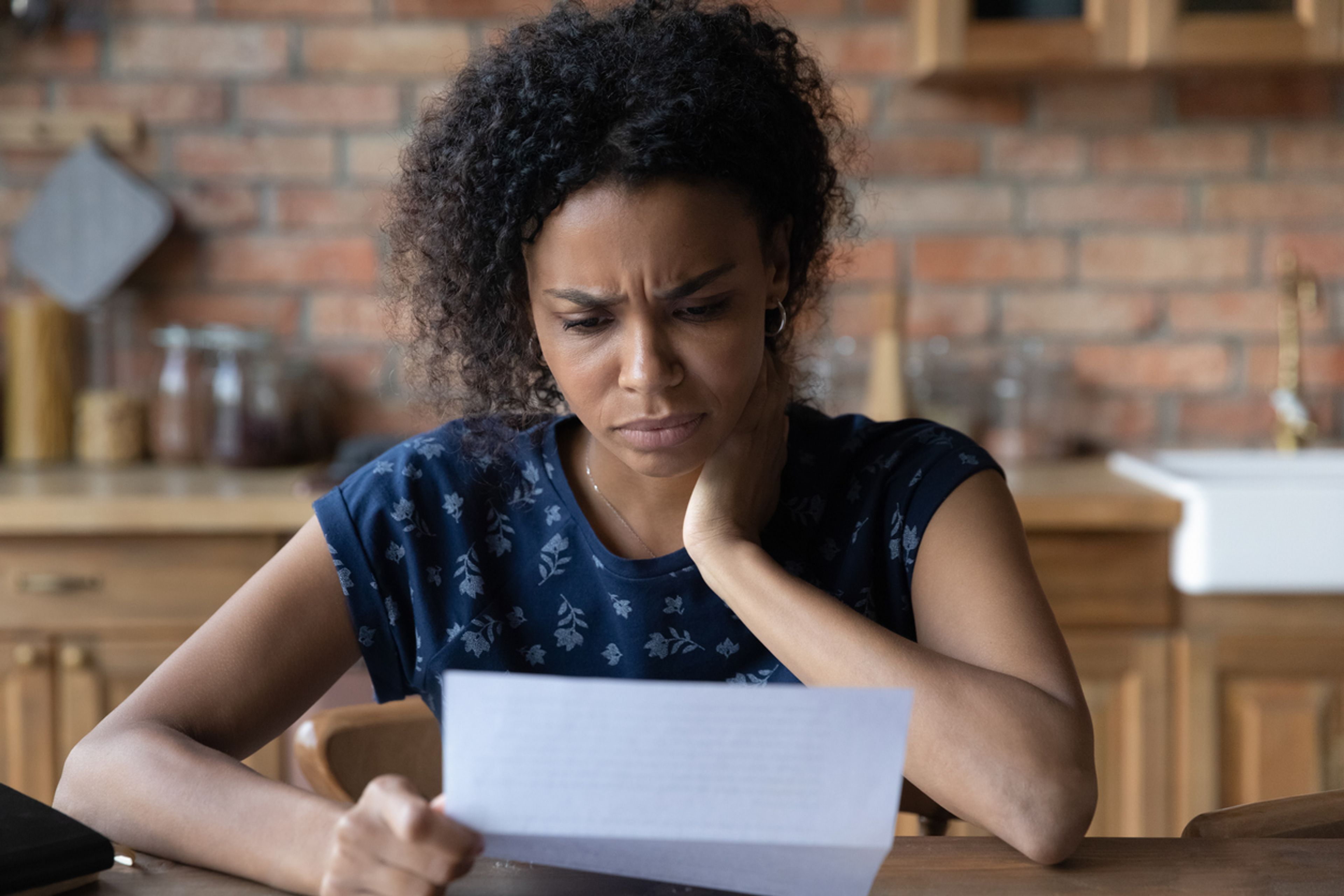 A woman reads a letter with her head propped on her hand and a confused look on her face.