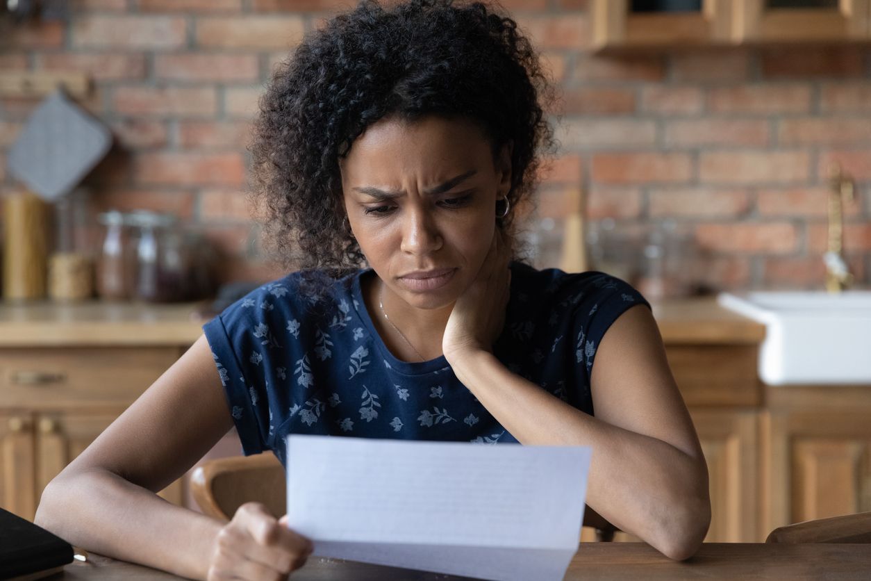 A woman reads a letter with her head propped on her hand and a confused look on her face.