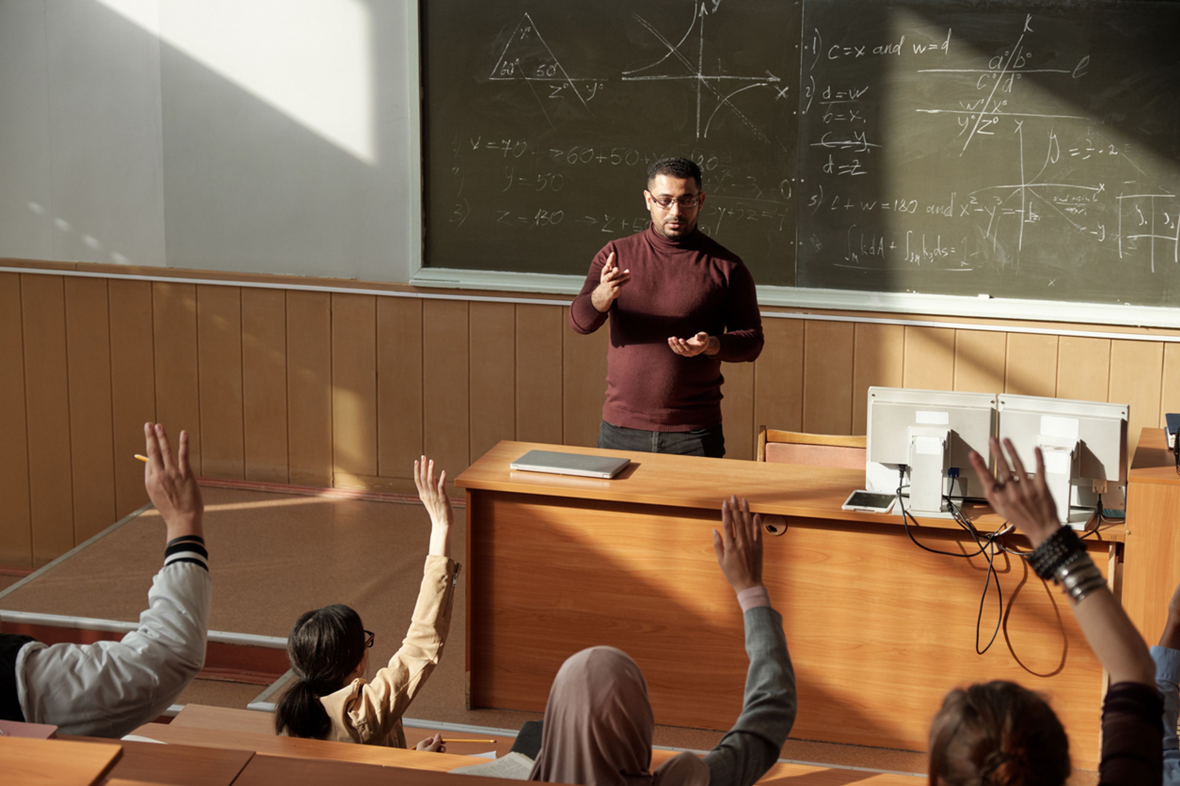 Professor teaching a class while standing in front of complex math equations on a chalkboard.