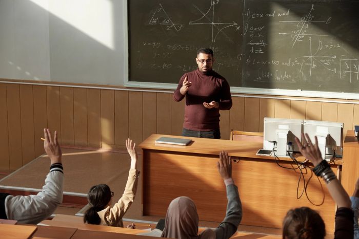 Professor teaching a class while standing in front of complex math equations on a chalkboard.