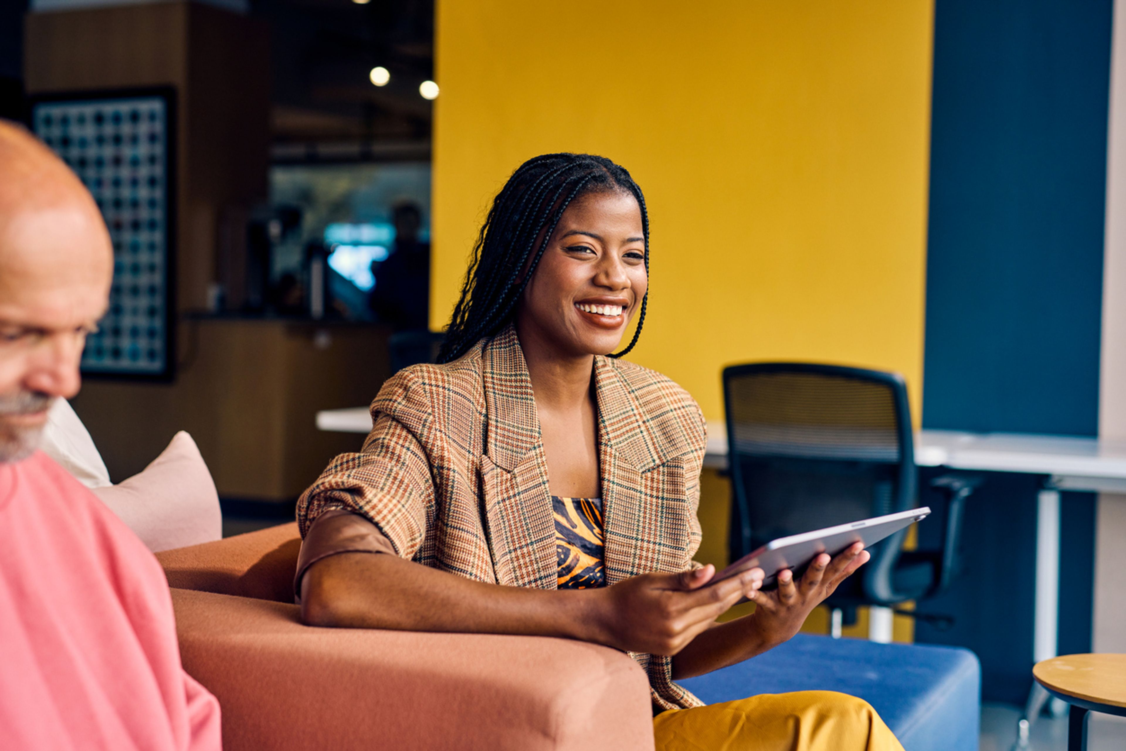 Business executive in colorful office reviewing information on a tablet and smiling.